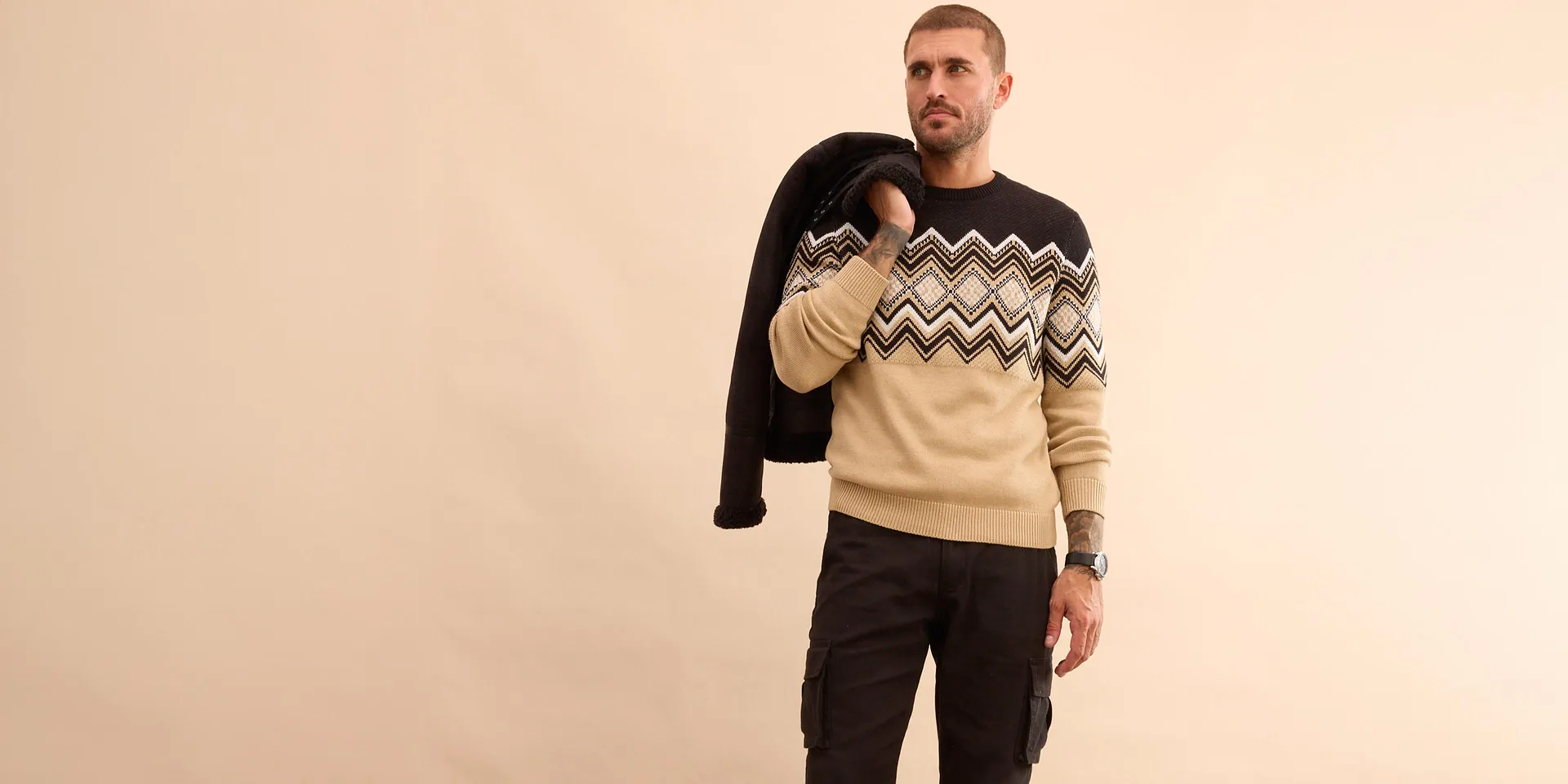 Stilvoller Look mit schwarzer Winterjacke, gemustertem Pullover und Jeans für kühle Tage.