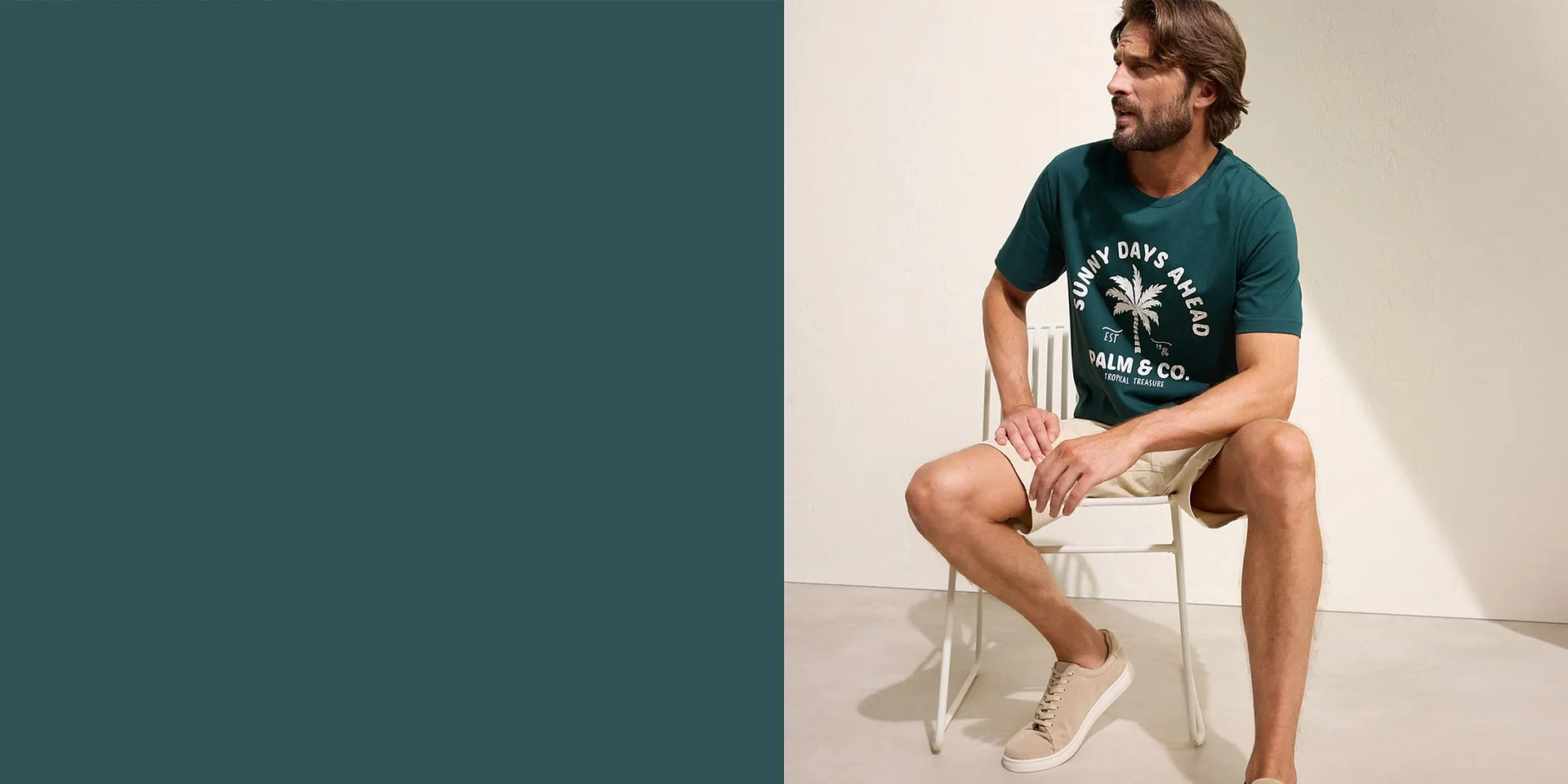 Mann trägt grünes T-Shirt mit Palmen-Print, beige Shorts und weiße Sneaker.