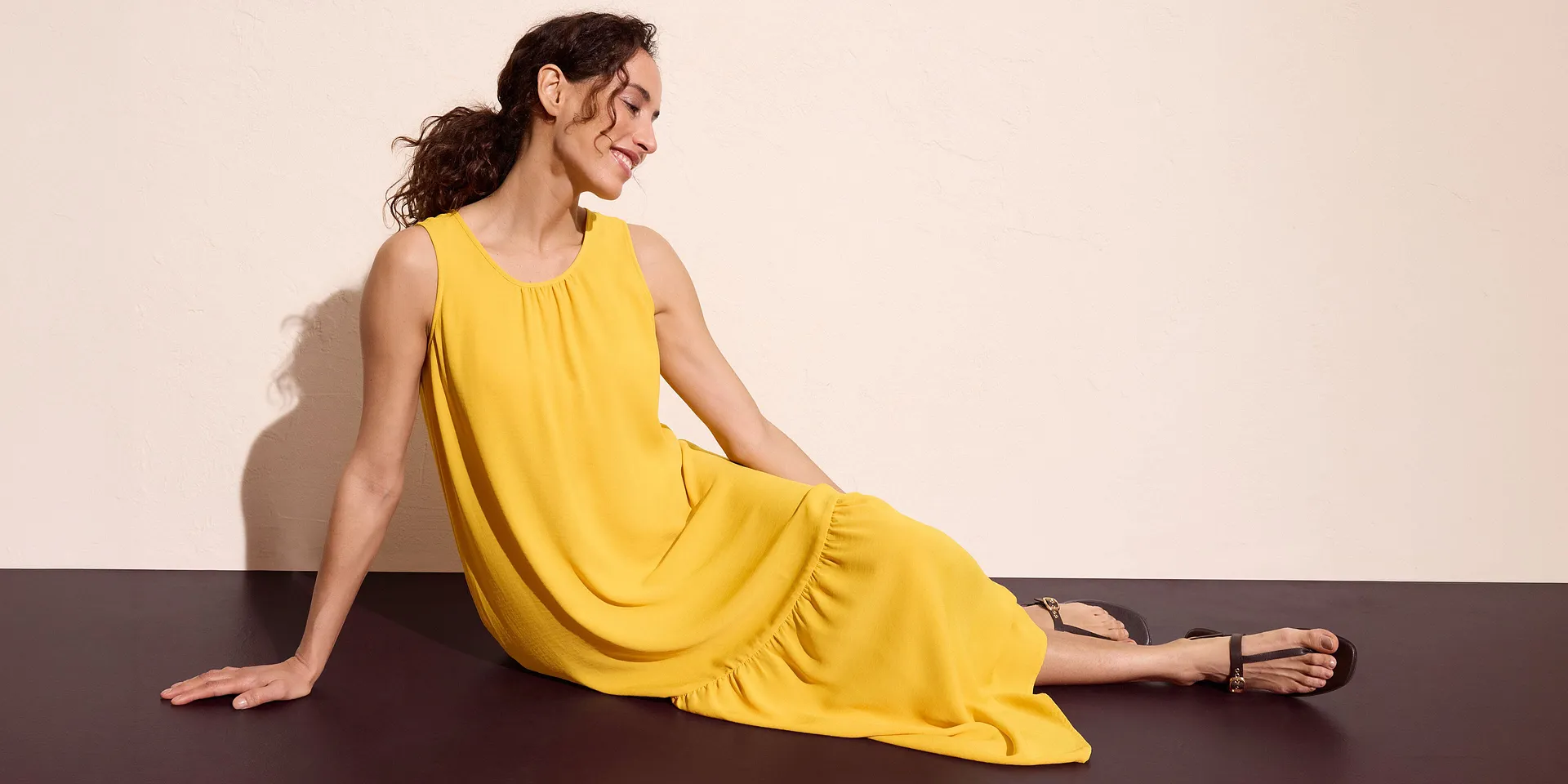 Gelbes ärmelloses Maxikleid kombiniert mit schwarzen Sandalen.