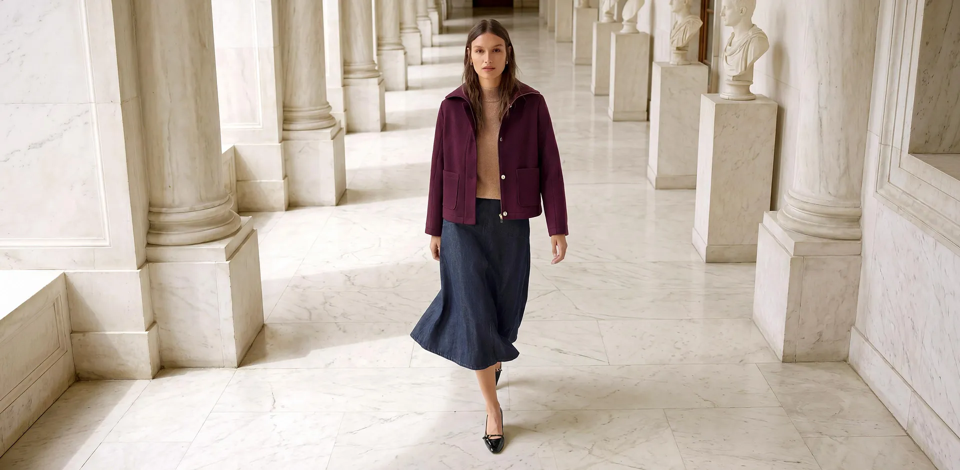 Bordeauxfarbene Jacke, beiger Pullover, dunkelblauer Jeansrock und schwarze Schuhe.