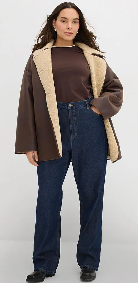 Veste marron à col clair, complétée d'un haut foncé et d'un jean.