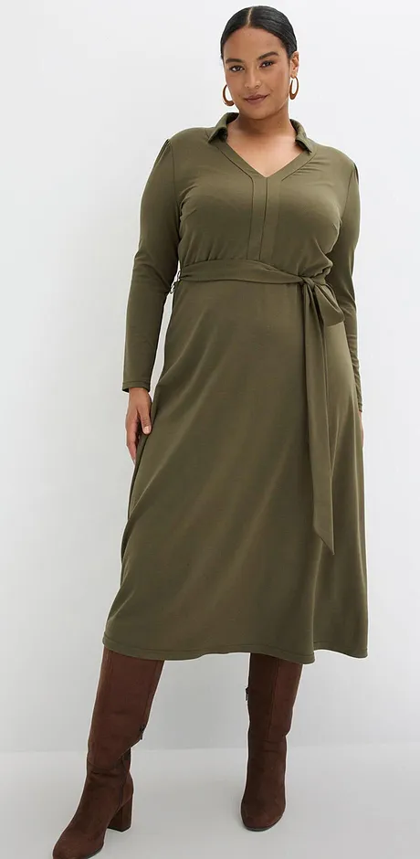 Robe vert olive avec décolleté en V et ceinture, associée à une paire de bottes marron.