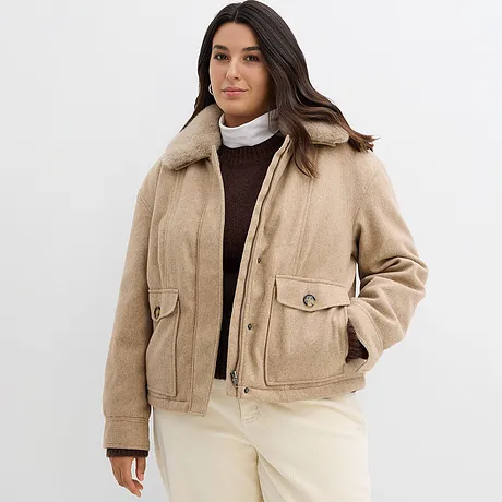 Veste d'hiver beige avec col, en-dessous un pull marron et un sous-pull à col roulé blanc.