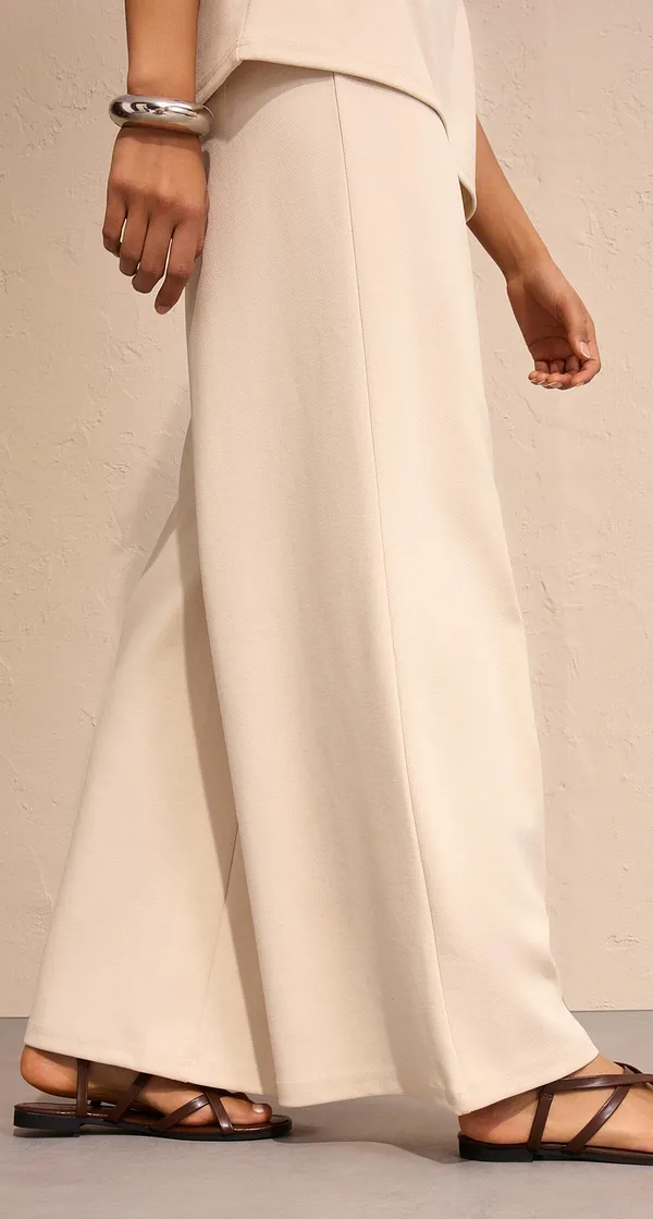 Elegante weite Hose in Cremeweiß, kombiniert mit flachen Sandalen.