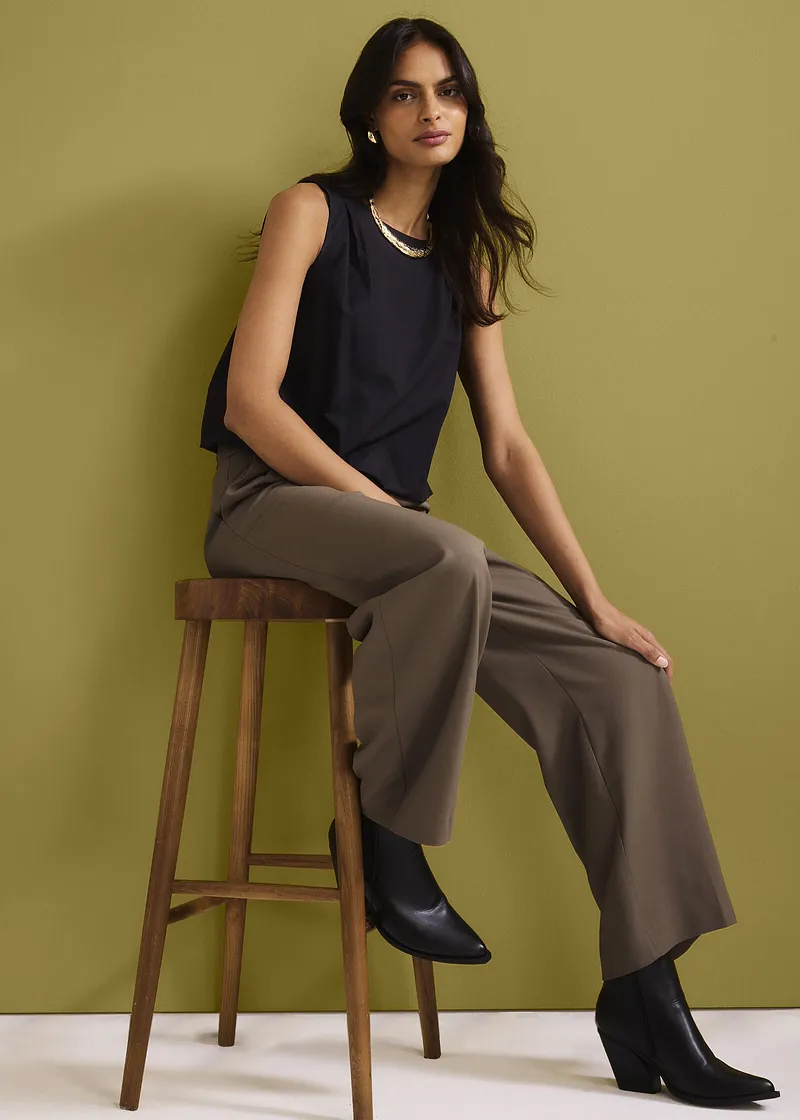 Dunkelblaues ärmelloses Top, weite braune Hose und schwarze Stiefeletten. Eleganter, lässiger Look.