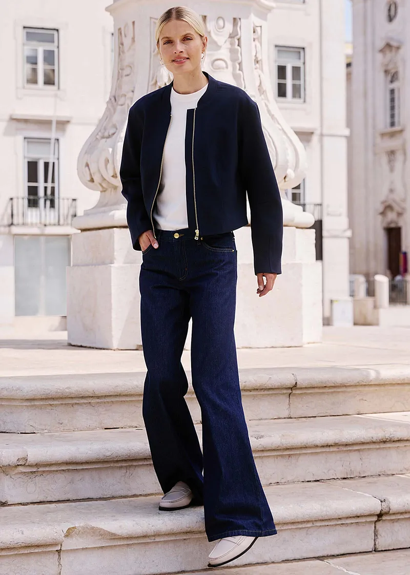 Eleganter Look mit dunkler Jacke, weißem Oberteil und weiten Jeans.
