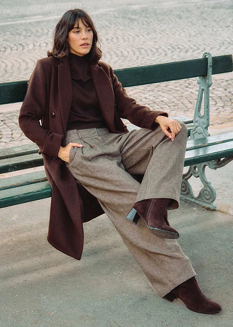 Manteau long marron, pull à col roulé et pantalon large en tweed.