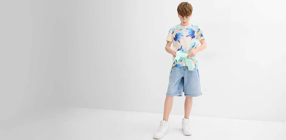 Buntes Kurzarmhemd mit T-Shirt, hellblaue Jeansshorts und weiße Sneakers.