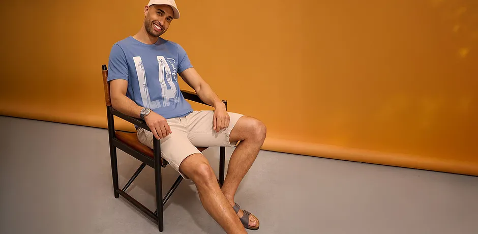 T-shirt bleu à imprimé, short clair, casquette et sandales.