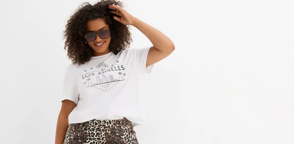 Lockeres weißes T-Shirt mit Aufdruck, kombiniert mit einem Rock im Leopardenmuster. Sonnenbrille als Accessoire.