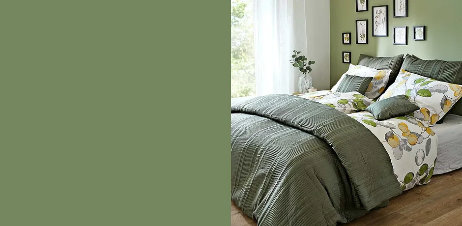 Gemütliches Schlafzimmer mit grüner Bettwäsche und Kissen. Blumenmuster auf der Bettwäsche bringen Frische.