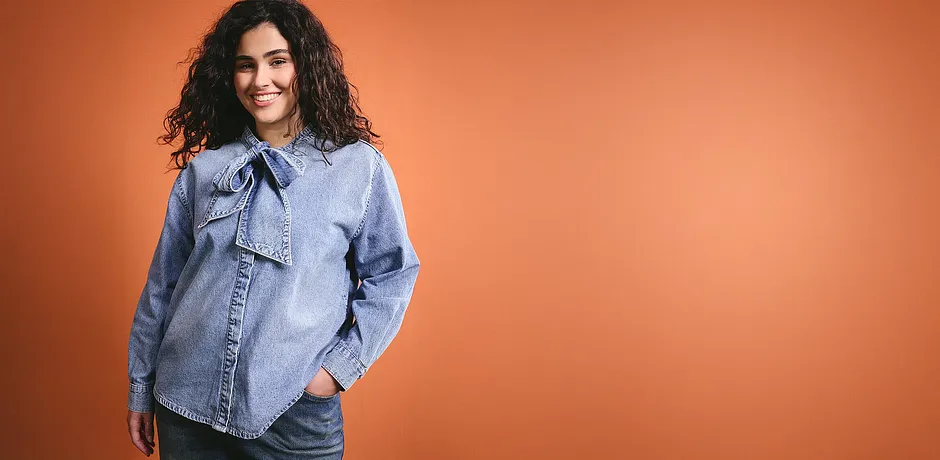Ein hellblaues Jeanshemd mit Schleife am Kragen verleiht dem Outfit einen lässigen Charme.