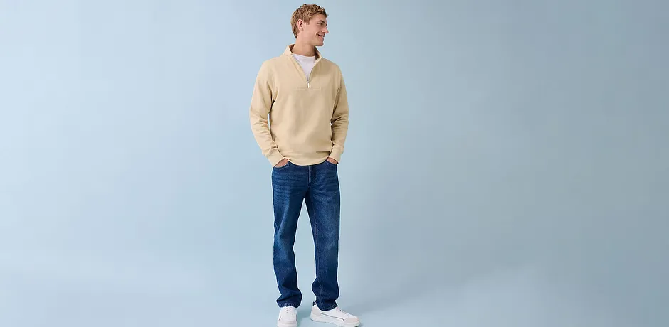Look décontracté avec pull couleur crème, jean bleu et baskets blanches.