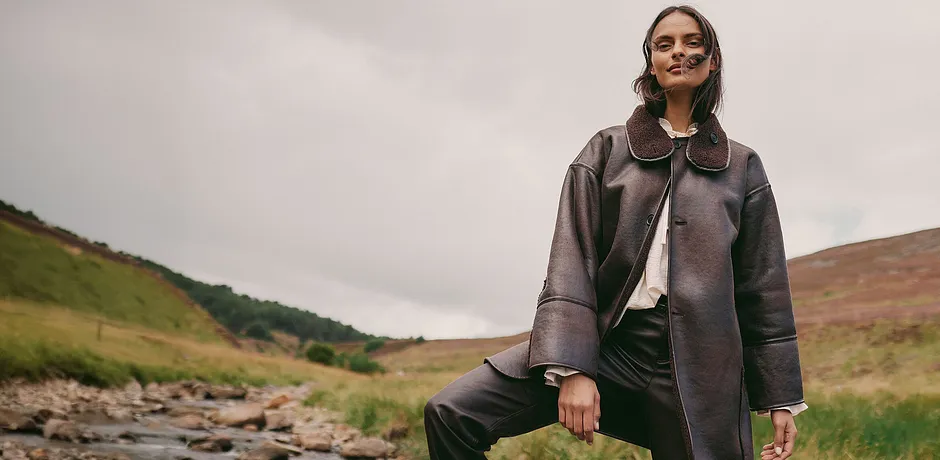 Manteau marron élégant avec grand col associé à un haut clair et un pantalon foncé.