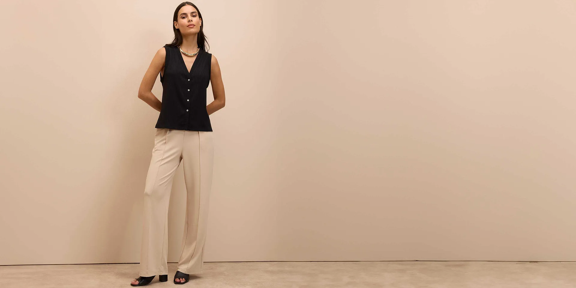 Elegante schwarze Weste mit Knöpfen, kombiniert mit weiten beigen Hosen und schwarzen Schuhen.