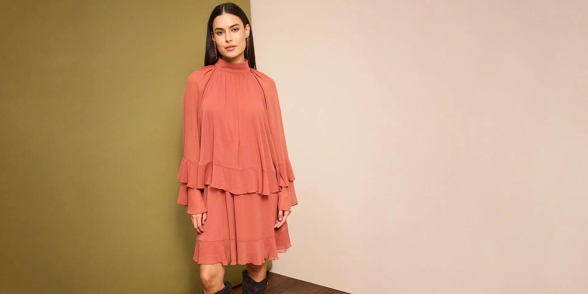 Ein lachsfarbenes Kleid mit Rüschen und weiten Ärmeln betont die feminine Silhouette.