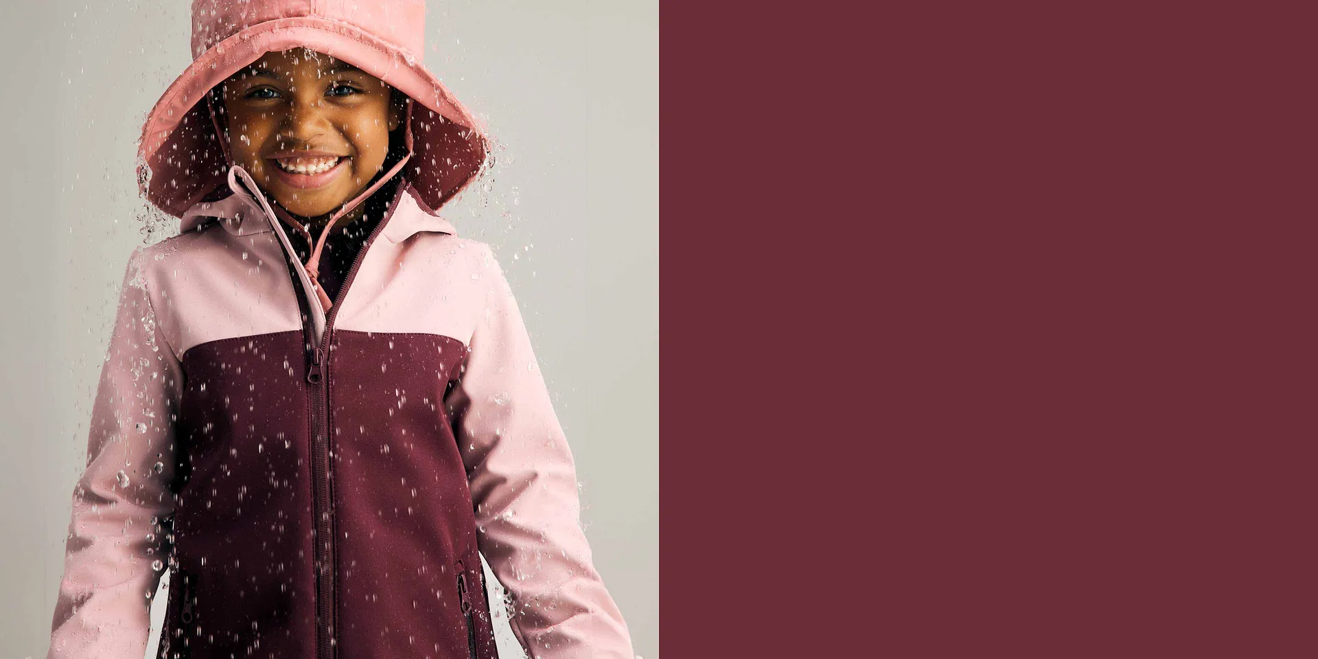 Regenjacke in Rosa und Bordeaux in Kombination mit einem Regenhut.