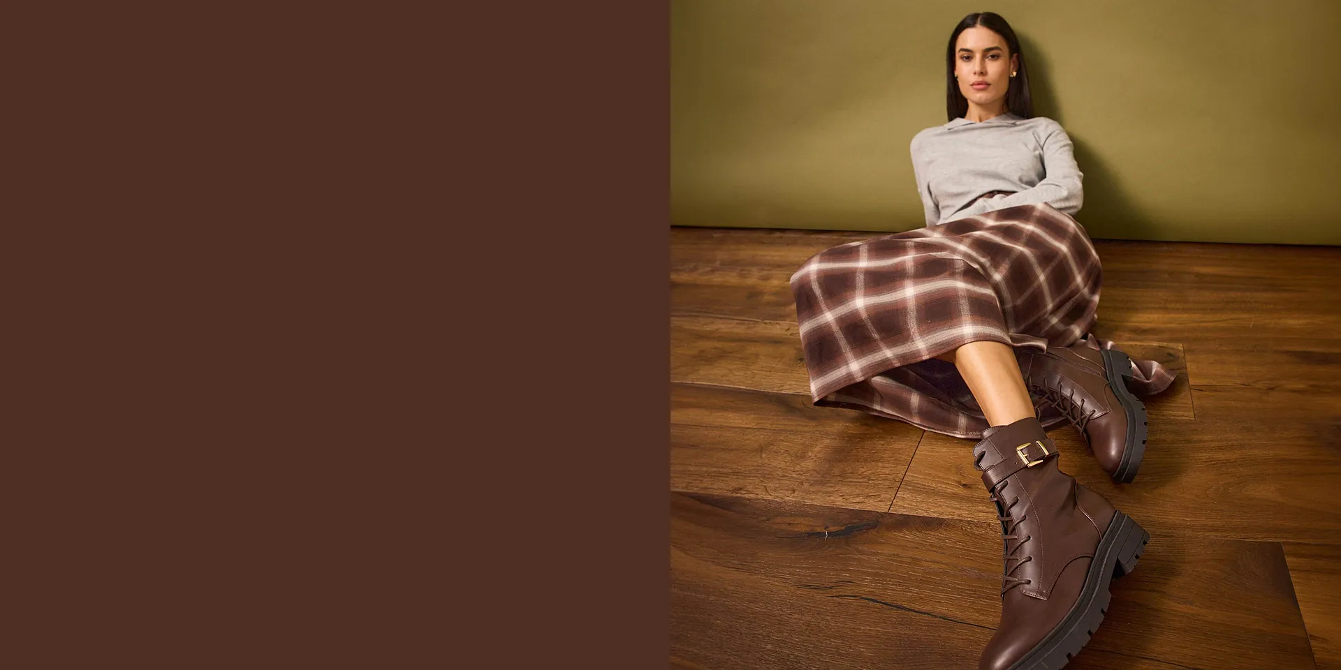 Grauer Pullover, karierter Rock und braune Lederstiefel.