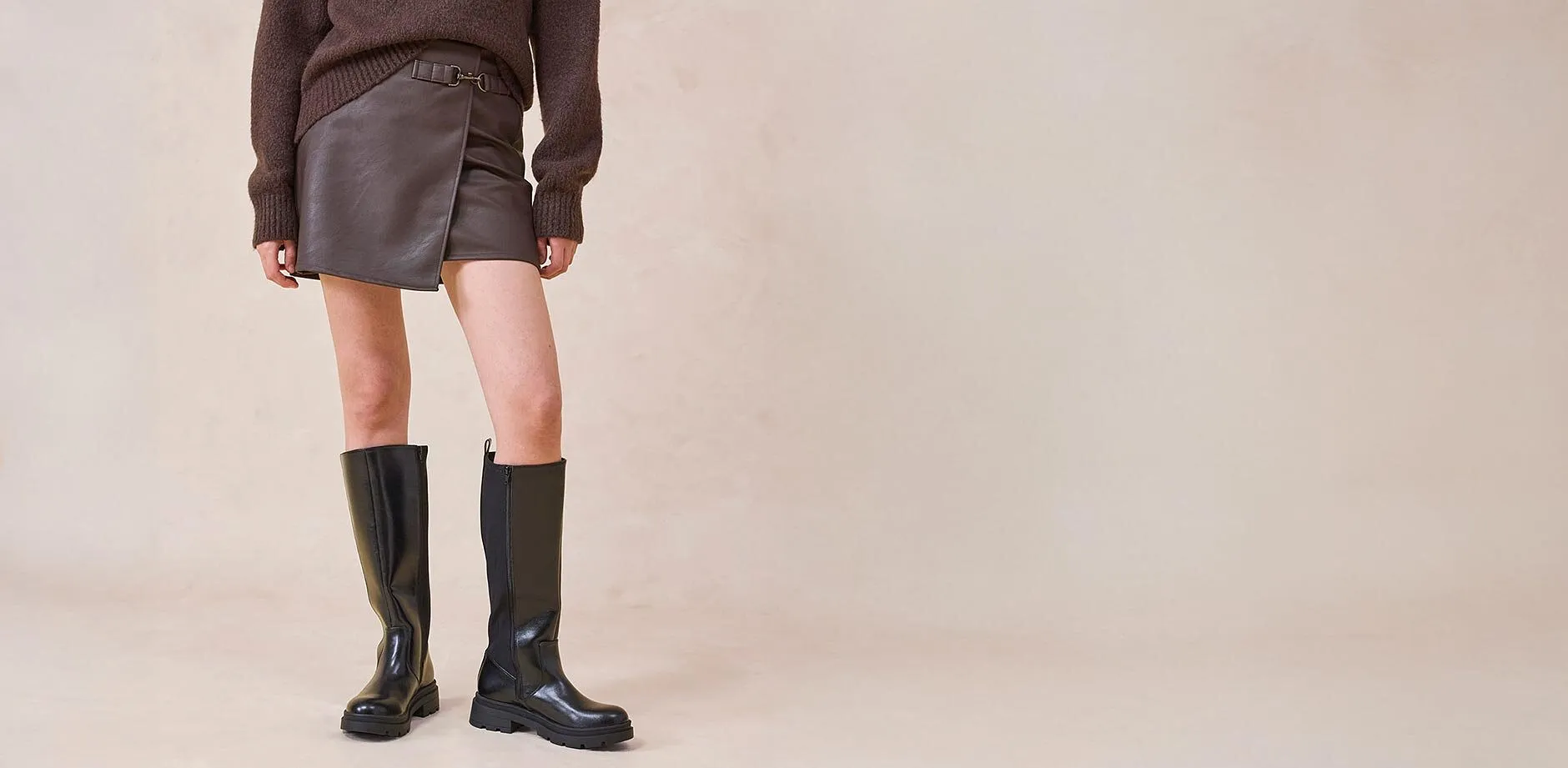 Lederrock und kniehohe Stiefel kombiniert mit einem braunen Pullover.