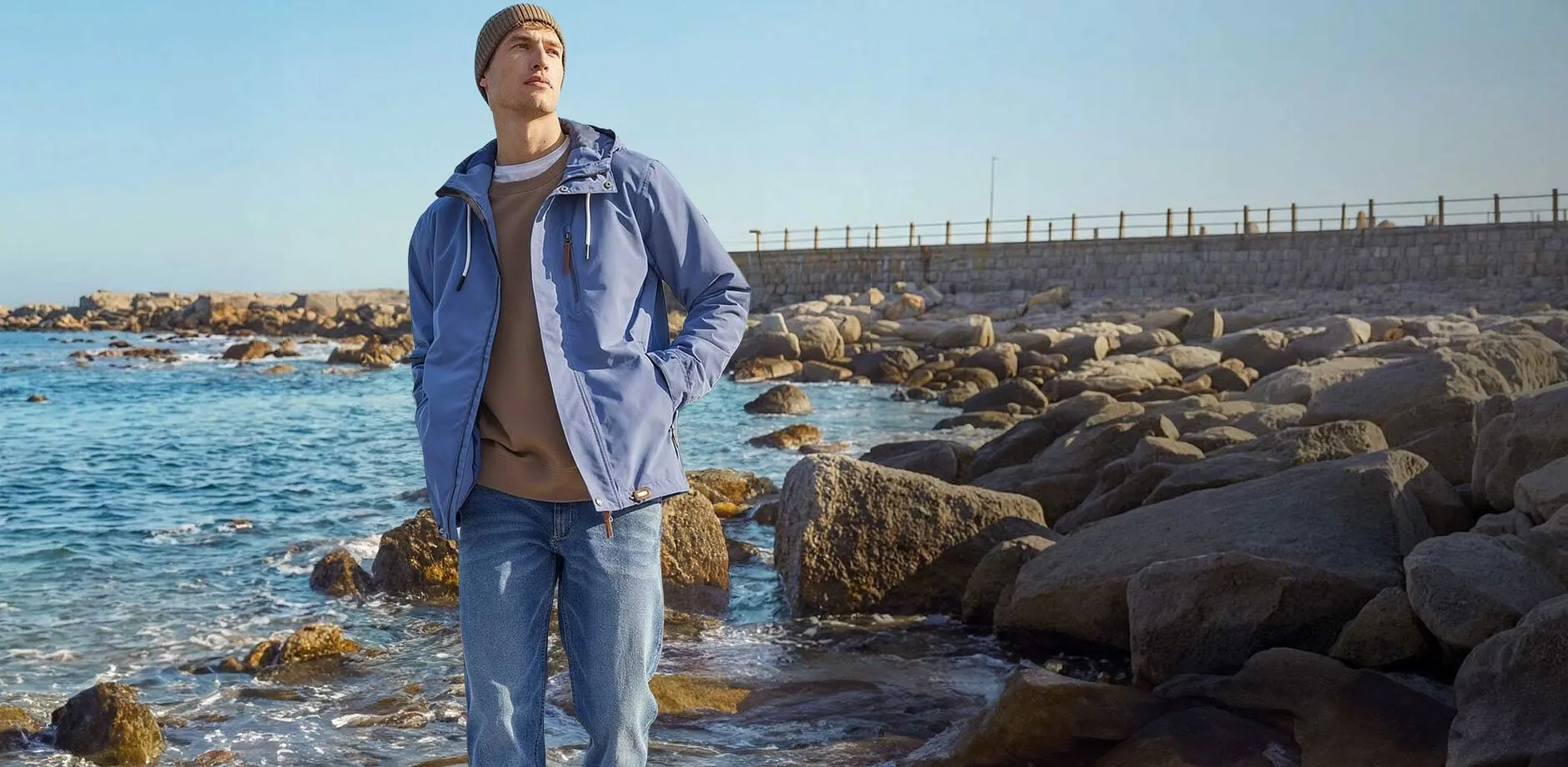 Stilvolle blaue Funktionsjacke und helle Jeans am Strand.