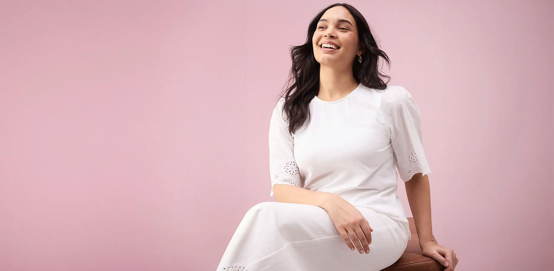  Eine strahlende Frau in einem schlichten wei&szlig;en Kleid mit kurzen &Auml;rmeln und Lochstickerei.