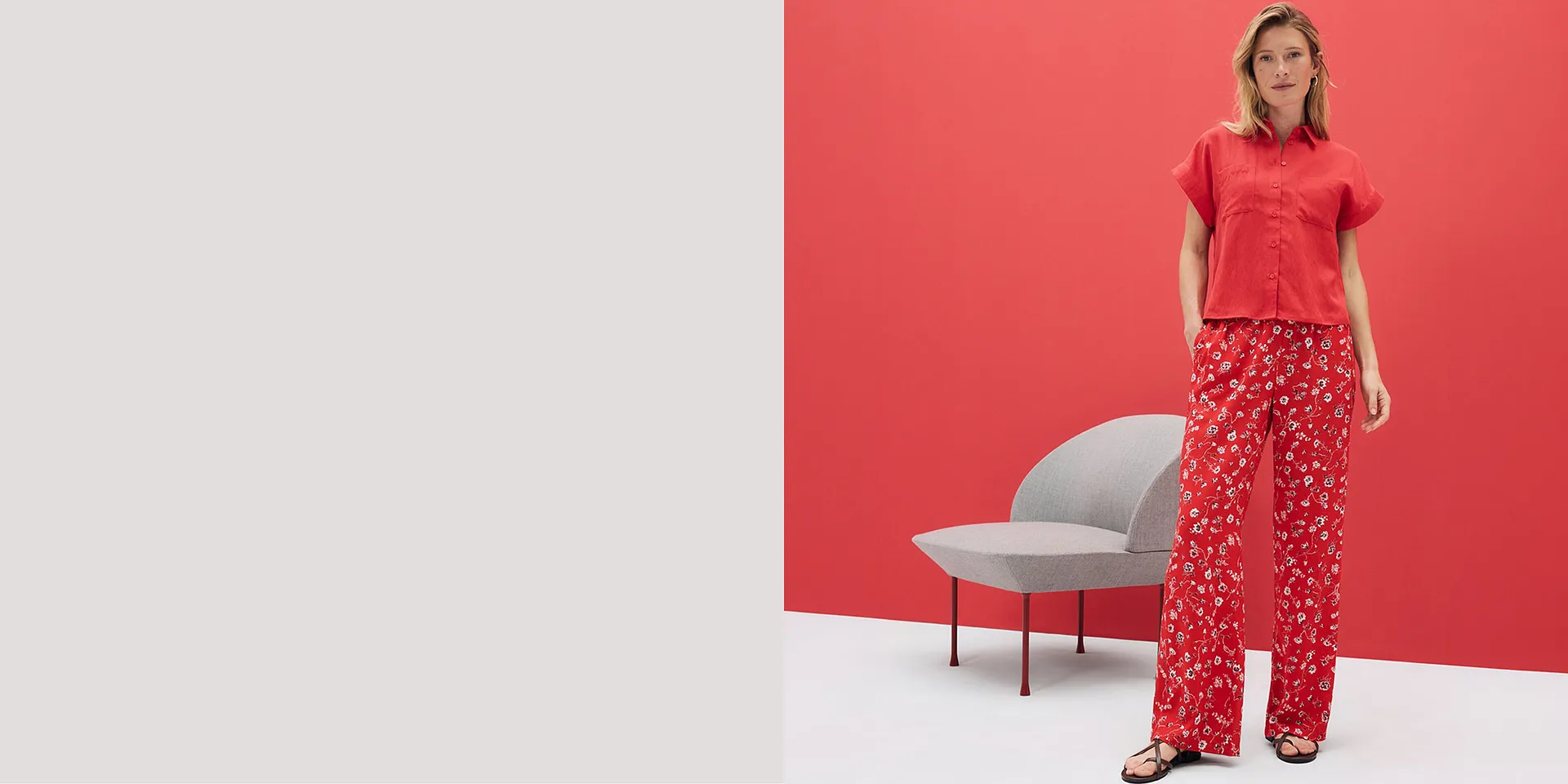 Rotes Kurzarm-Hemd und flie&szlig;ende Hose mit floralem Muster. Sommerliches Outfit vor leuchtend rotem Hintergrund.