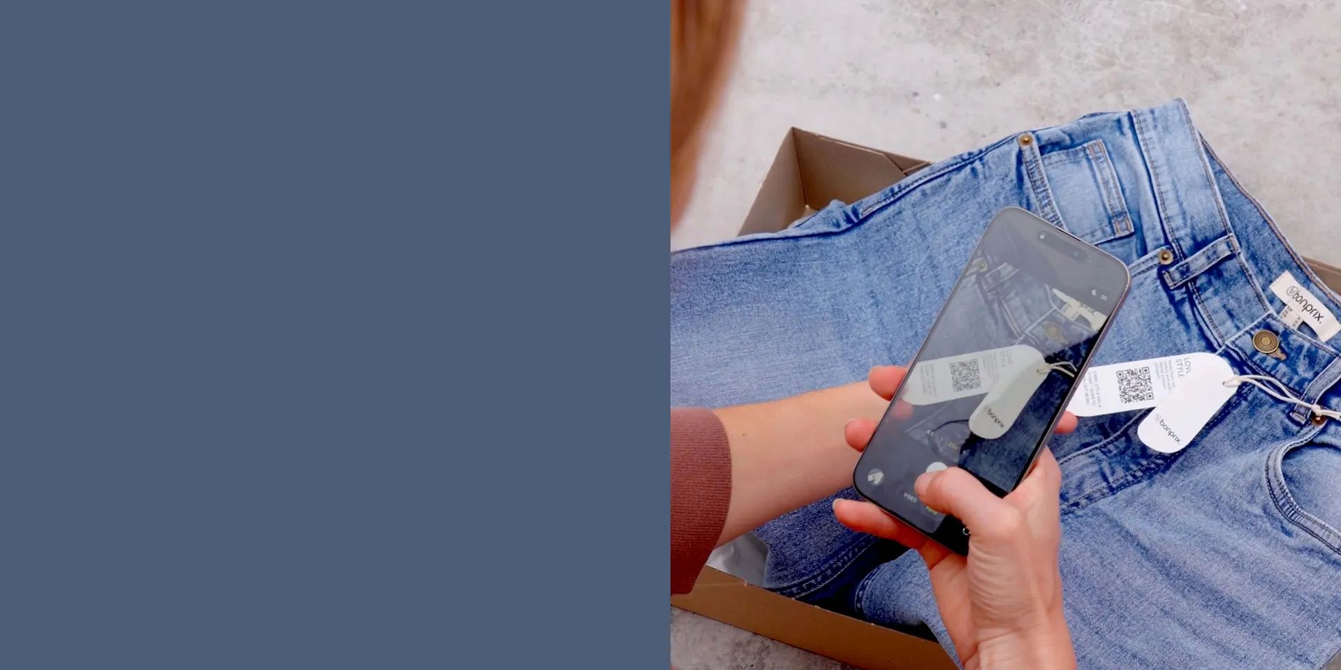 Blaue Jeans auf grauem Untergrund. H&auml;nde halten Smartphone &uuml;ber der Kleidung.