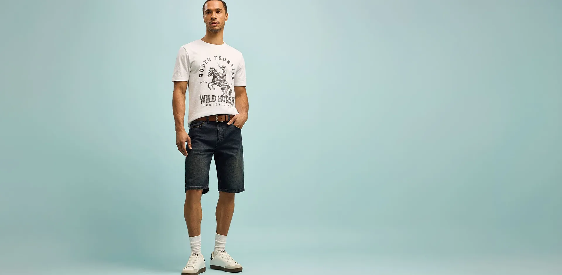 Homme v&ecirc;tu d'un T-shirt blanc &agrave; imprim&eacute; et d'un short fonc&eacute; dans une pose d&eacute;contract&eacute;e. 