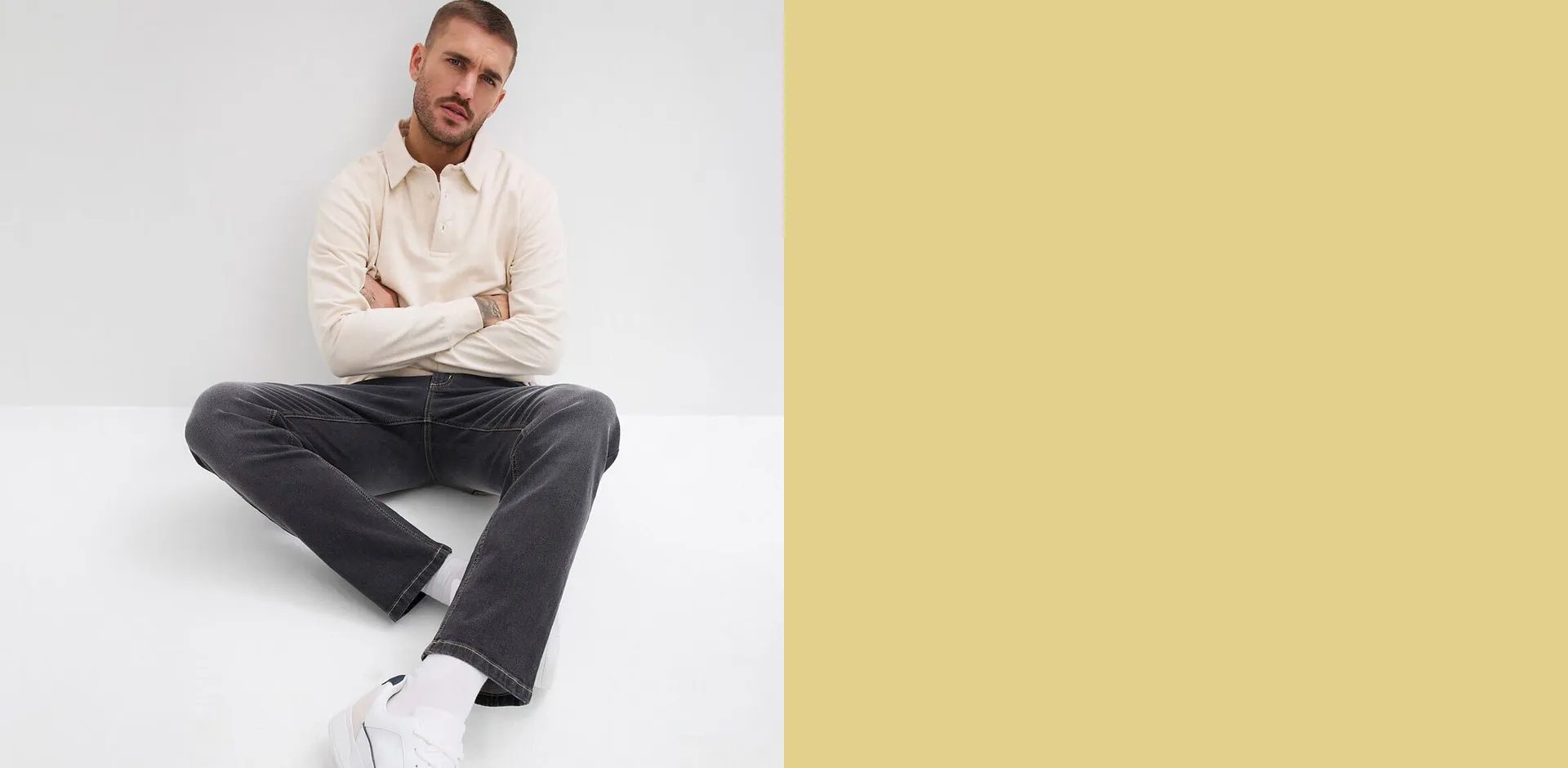 Un homme portant un T-shirt de couleur cr&egrave;me, un pantalon gris fonc&eacute; et des sneakers blanches.