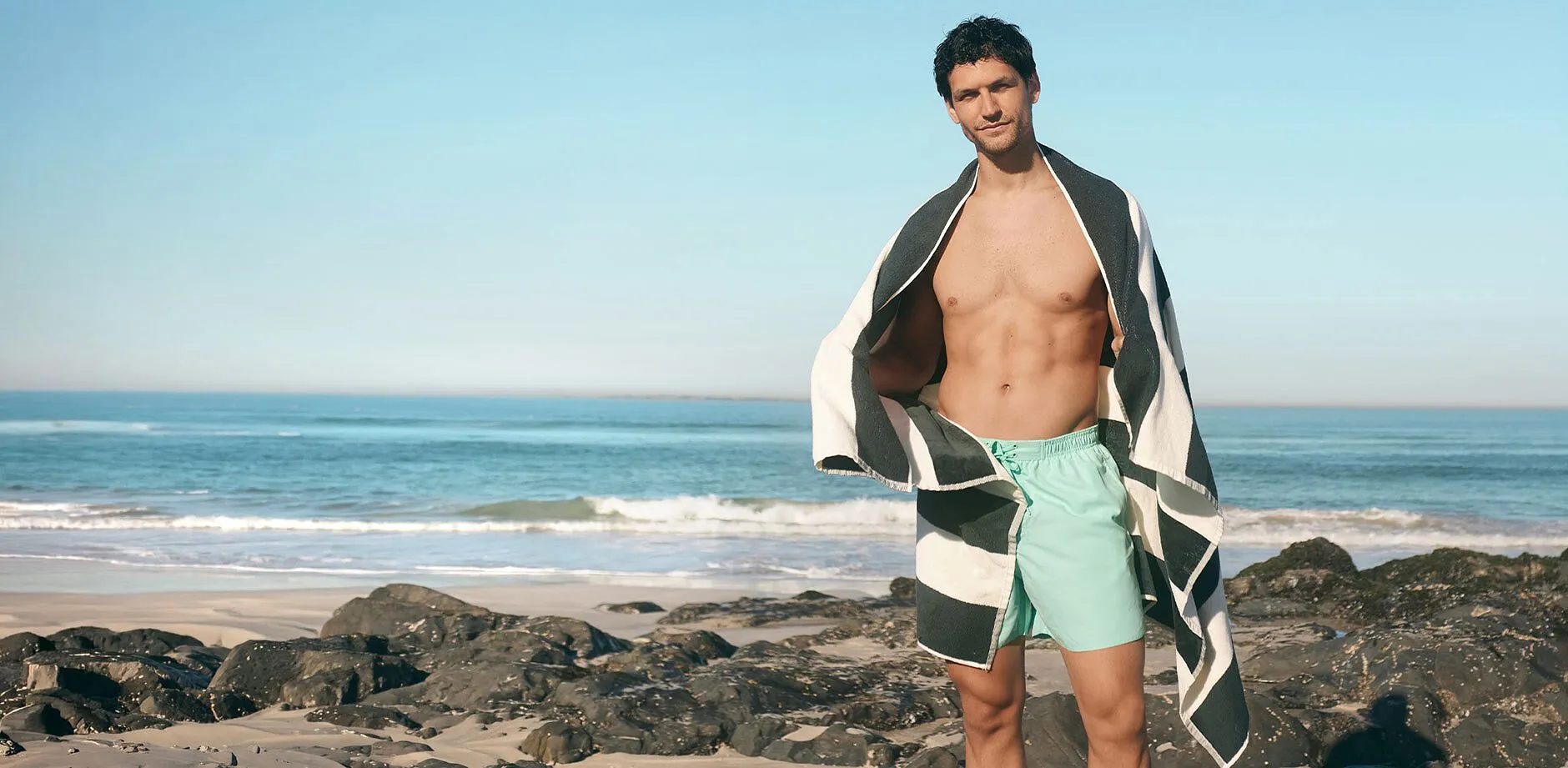 Un homme v&ecirc;tu d'un maillot de bain vert menthe et portant un drap de plage &agrave; rayures tendance sur les &eacute;paules.