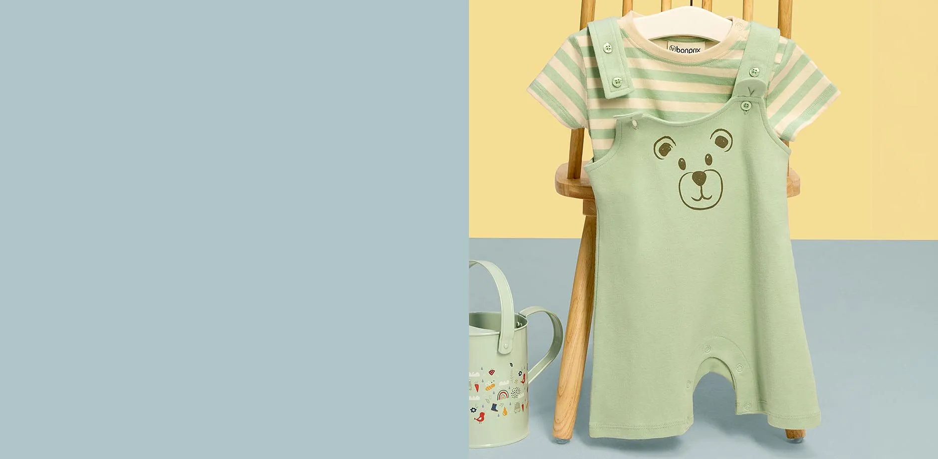 S&uuml;&szlig;e mintgr&uuml;ne Baby-Latzhose mit B&auml;renmotiv und gestreiftem T-Shirt an Holzstuhl aufgeh&auml;ngt.