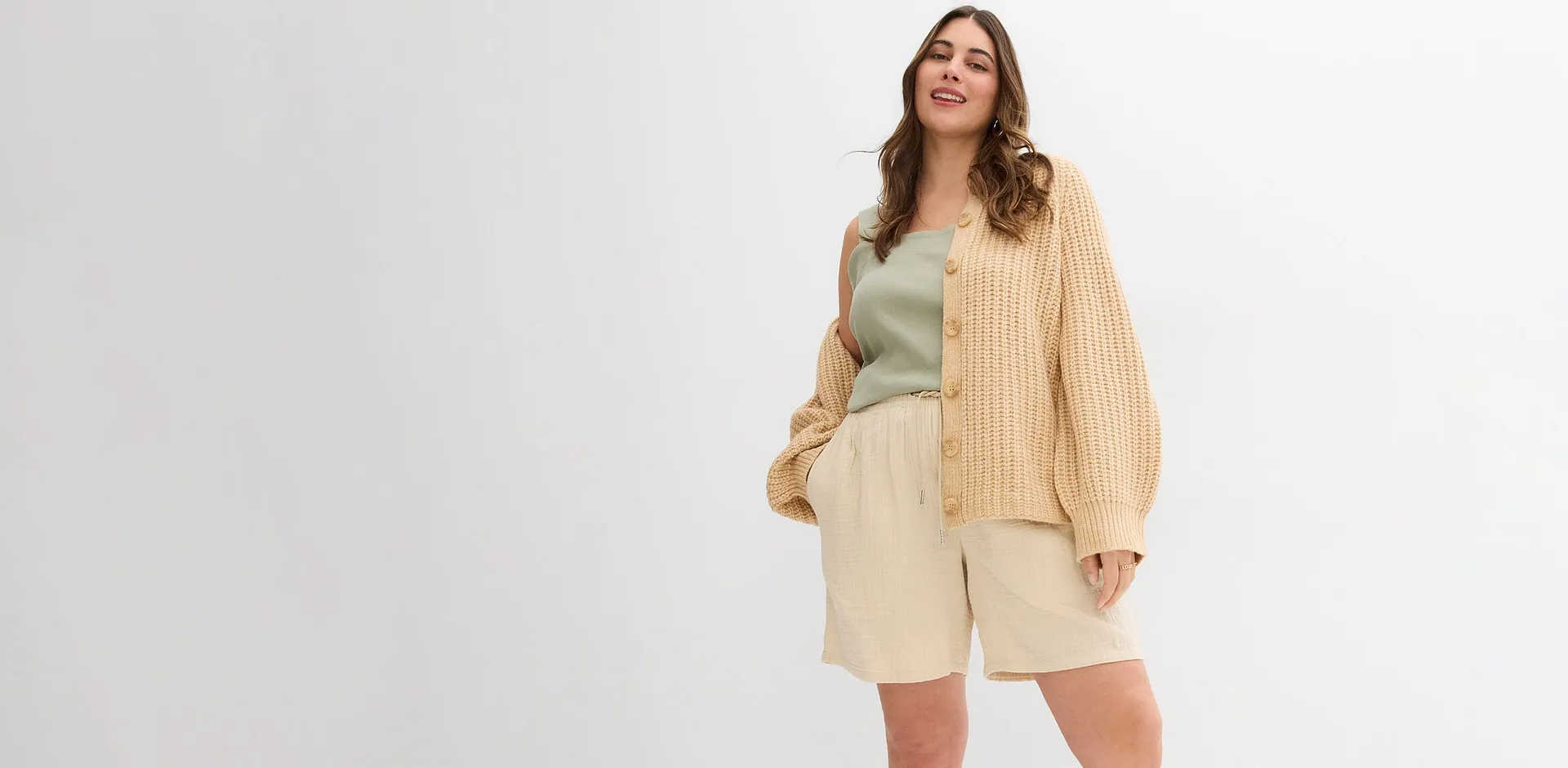 Une femme v&ecirc;tue d'un cardigan beige, un top vert clair et un short couleur cr&egrave;me.