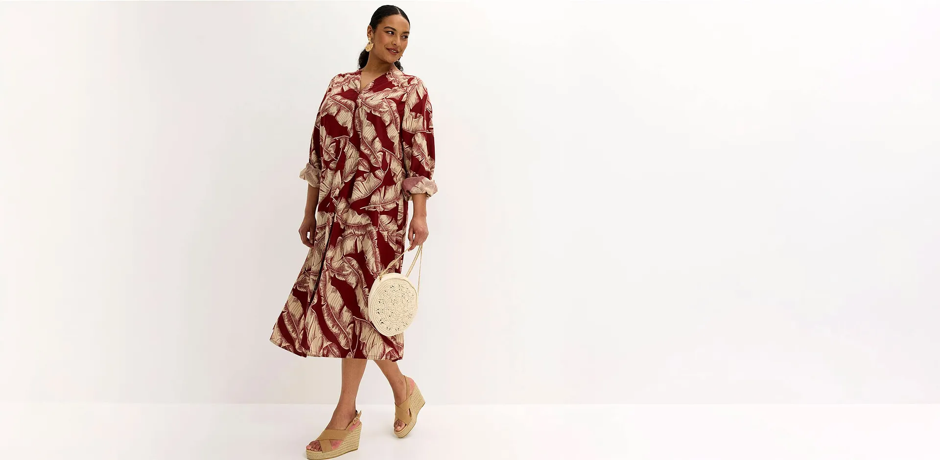 Robe midi &agrave; imprim&eacute; botanique en rouge et beige, associ&eacute;e &agrave; un sac &agrave; main tress&eacute; et des chaussures compens&eacute;es.