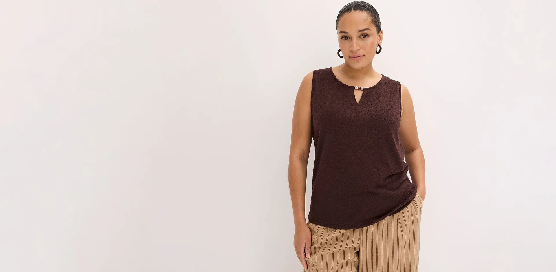 Une femme v&ecirc;tue d'un haut marron sans manches et d'un pantalon ray&eacute; beige.