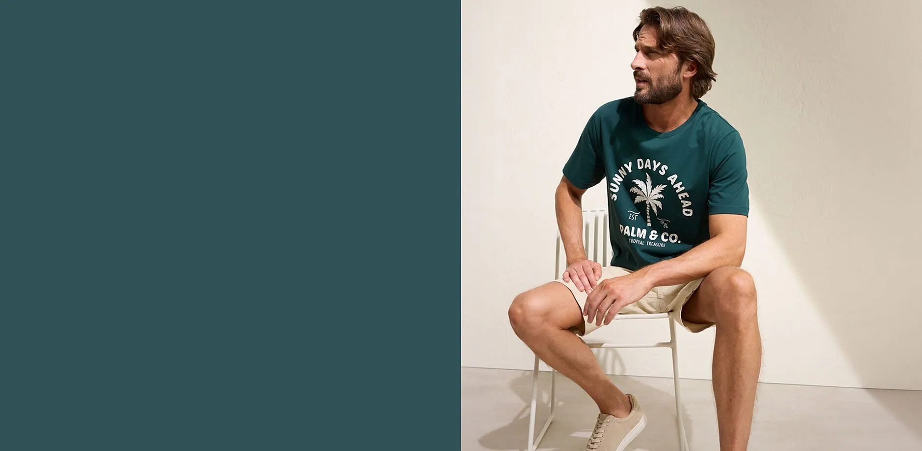 Un homme v&ecirc;tu d'un T-shirt vert &agrave; imprim&eacute; palmiers, d'un short beige et de sneakers blanches.
