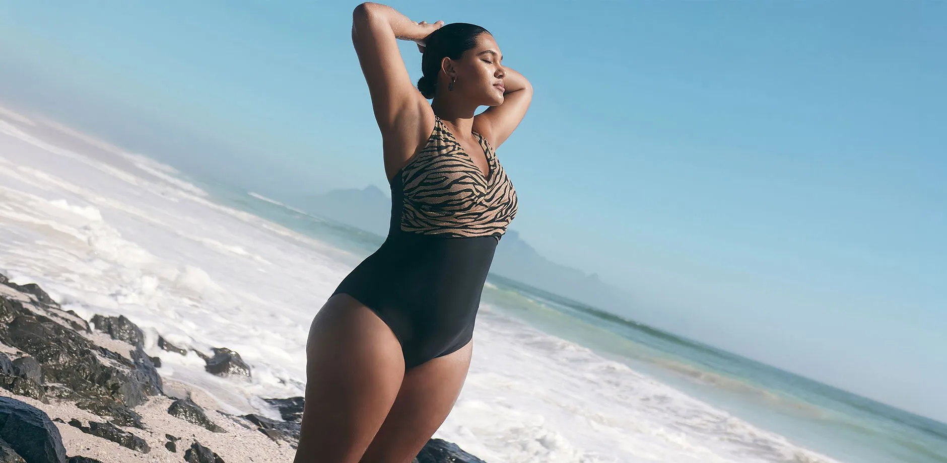 Maillot 1 pi&egrave;ce avec partie sup&eacute;rieure &agrave; imprim&eacute; tigr&eacute; et partie inf&eacute;rieure noir uni sur la plage.