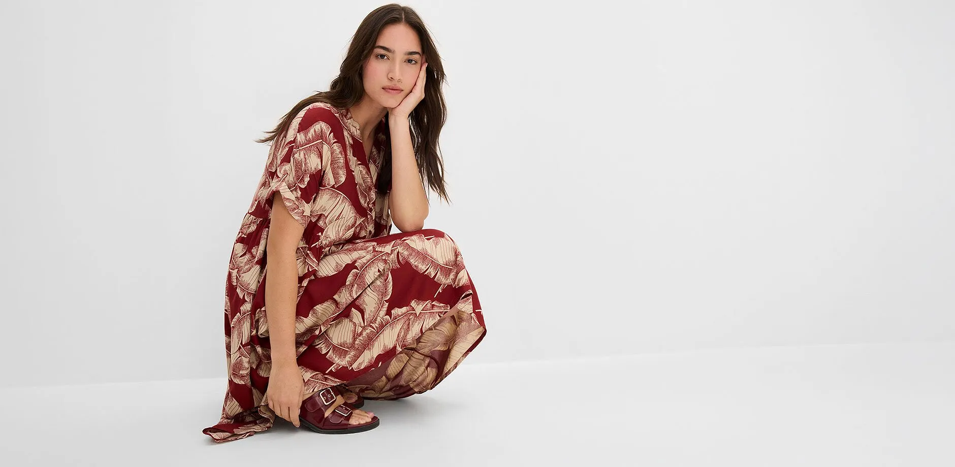 Robe caftan longueur midi de couleur bordeaux avec un motif v&eacute;g&eacute;tal dor&eacute; et des sandales assorties.