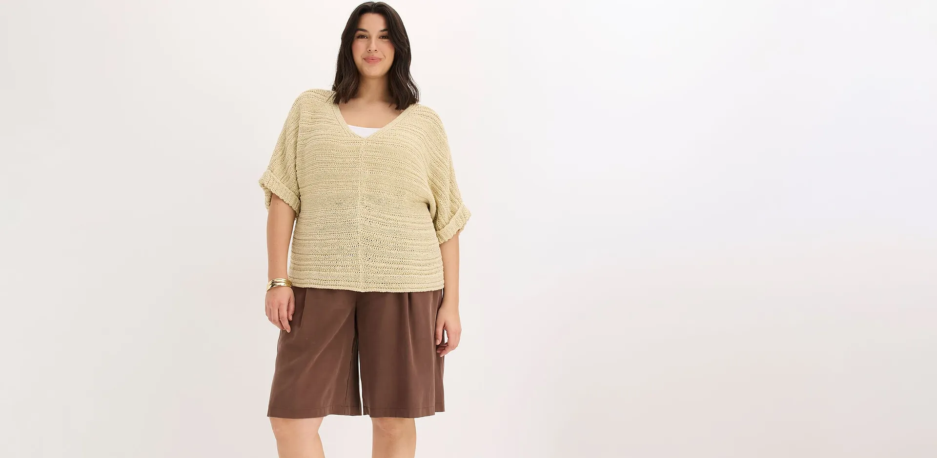 Une femme portant un haut en maille beige et un bermuda large marron.