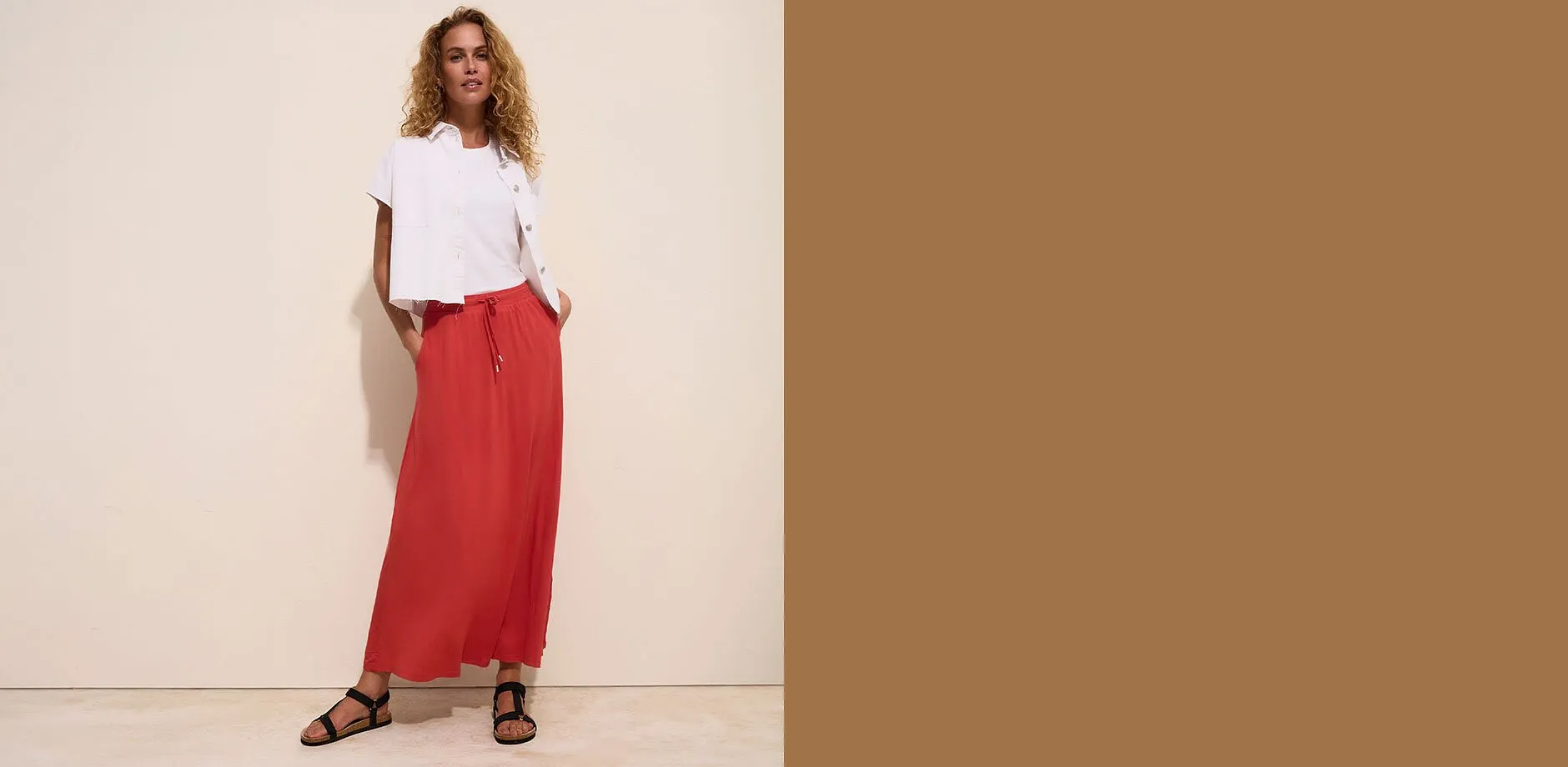 Veste blanche d&eacute;contract&eacute;e, T-shirt blanc et jupe longue rouge avec sandales noires.