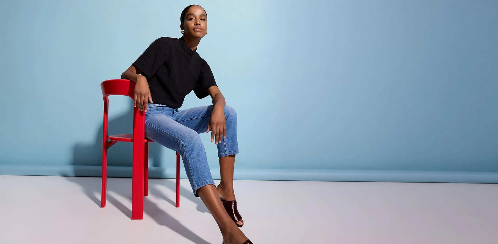 Outfit mit schwarzem Oberteil, blauen Jeans und gl&auml;nzenden Mules.