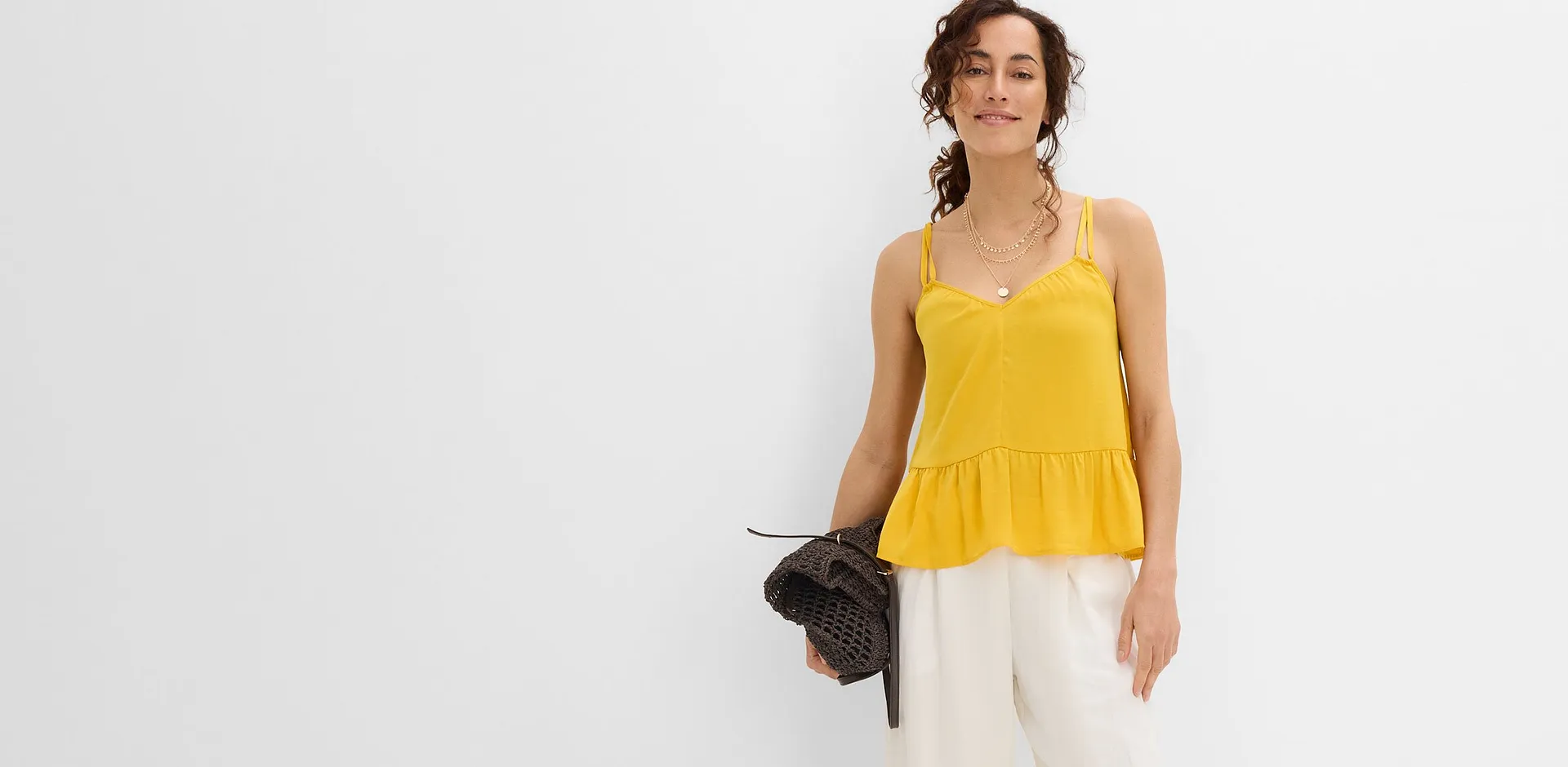 Top jaune &agrave; bretelles, pantalon large blanc et sac marron.