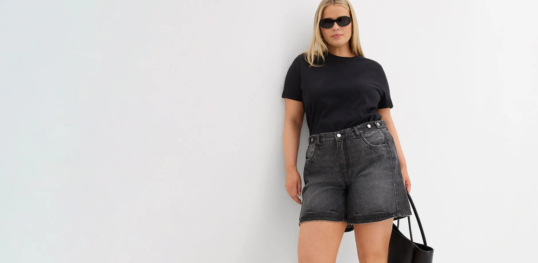 T-shirt noir, short en jean gris de coupe large, lunettes de soleil et sac noir.