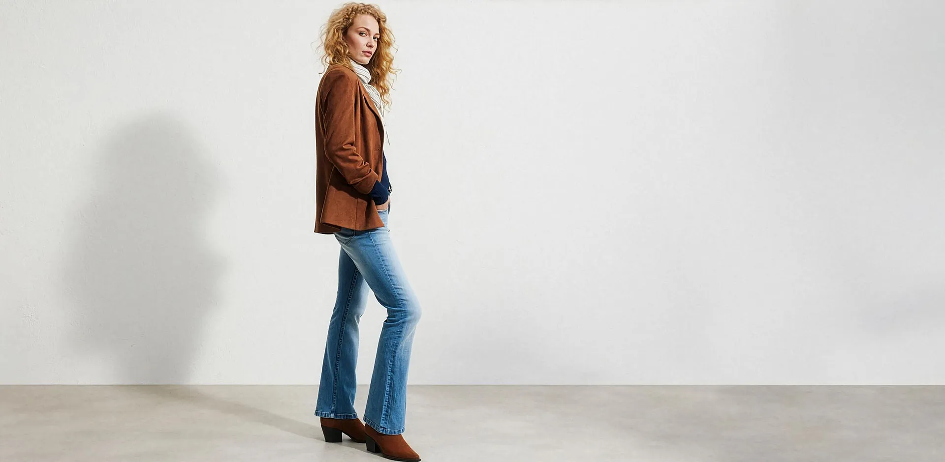 Veste en daim marron, jean &agrave; patte d'eph, pull blanc &agrave; col roul&eacute; et bottines marron.