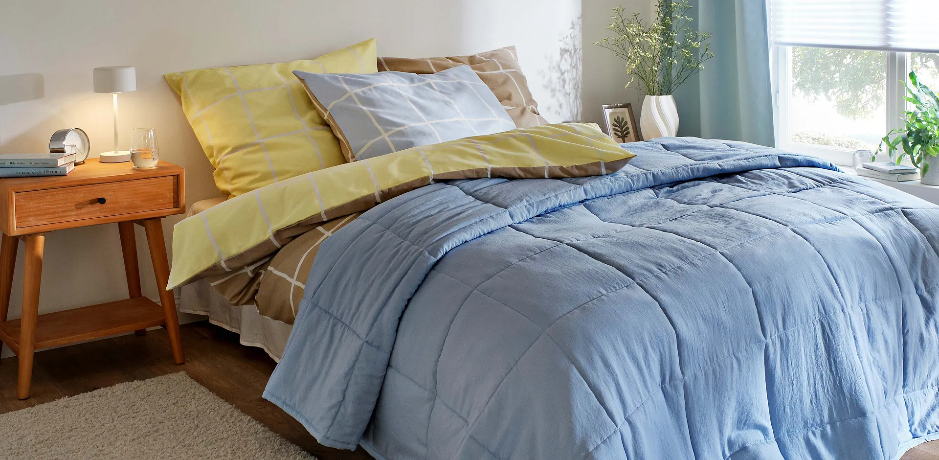 Schlafzimmer mit hellblauer Tagesdecke, gelben Kissen und Bettw&auml;sche.