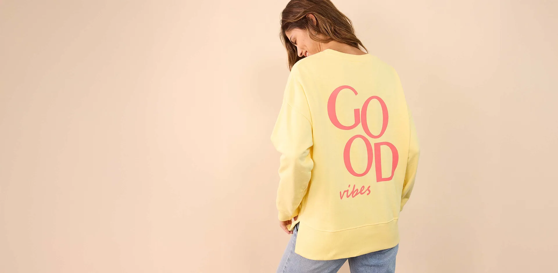Gelber Oversize-Pullover mit rosa "Good vibes"-Aufdruck auf dem R&uuml;cken.