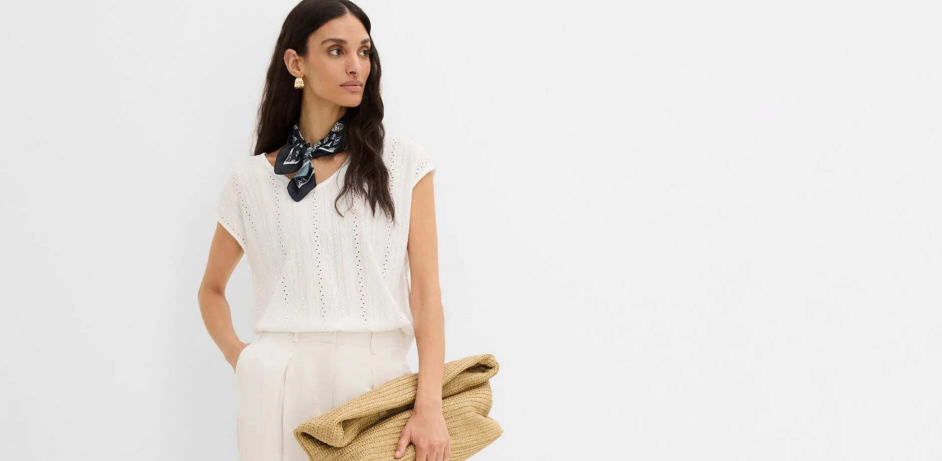 Blouse blanche &agrave; motif ajour&eacute;, pantalon clair, foulard fonc&eacute; et pochette en paille.