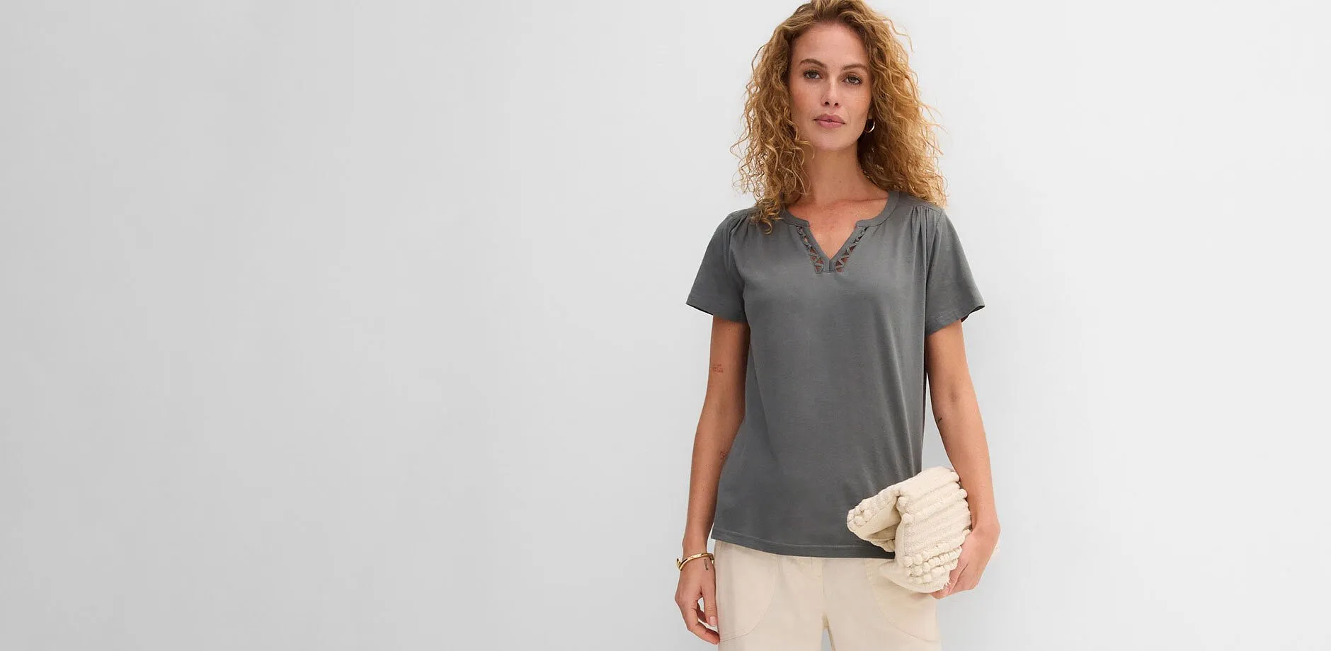 T-shirt gris avec d&eacute;collet&eacute; en V, pantalon clair et pochette structur&eacute;e beige.