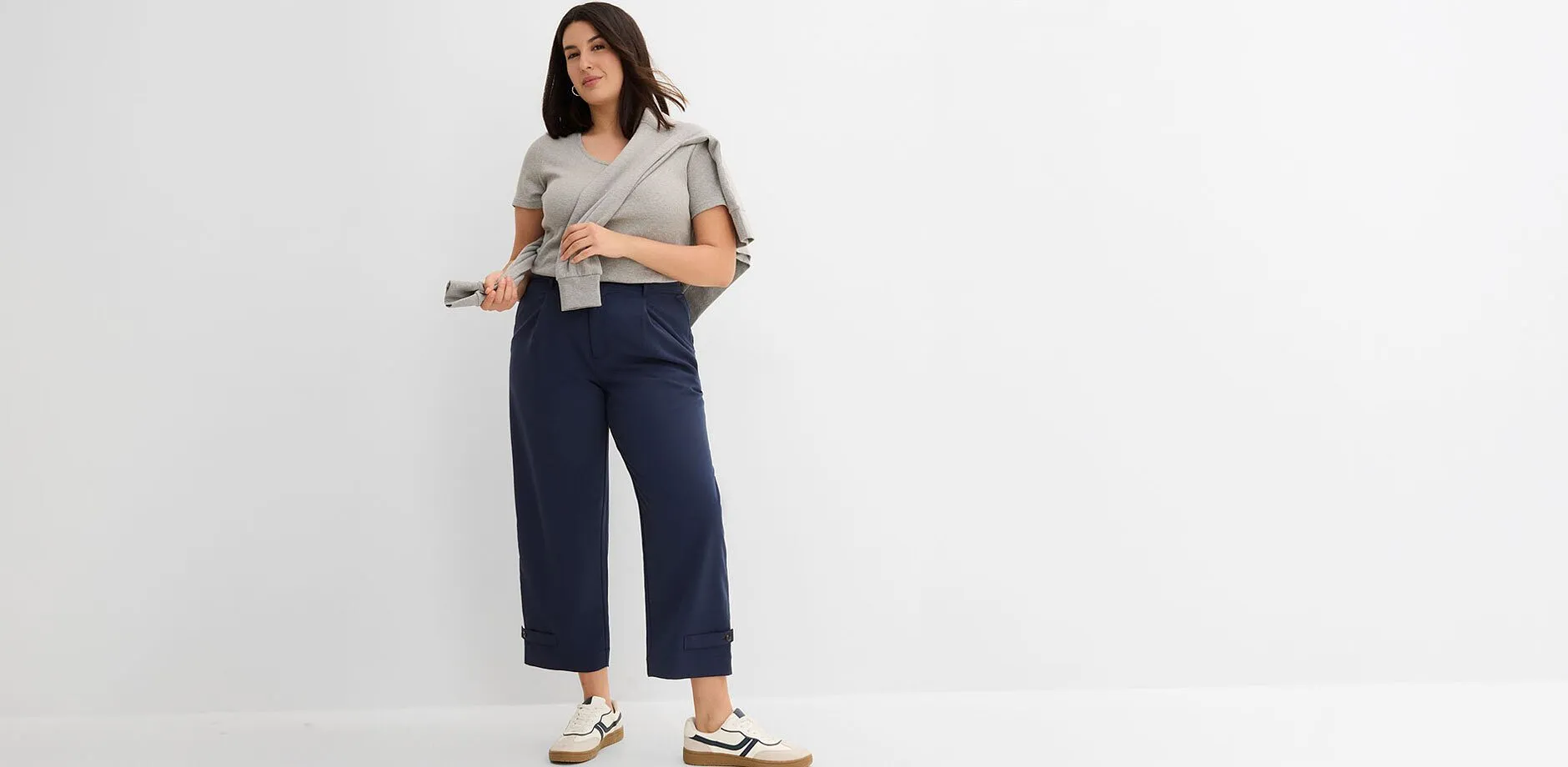 T-shirt gris, pantalon bleu marine avec empi&egrave;cement &agrave; la taille, pull et sneakers blanches.