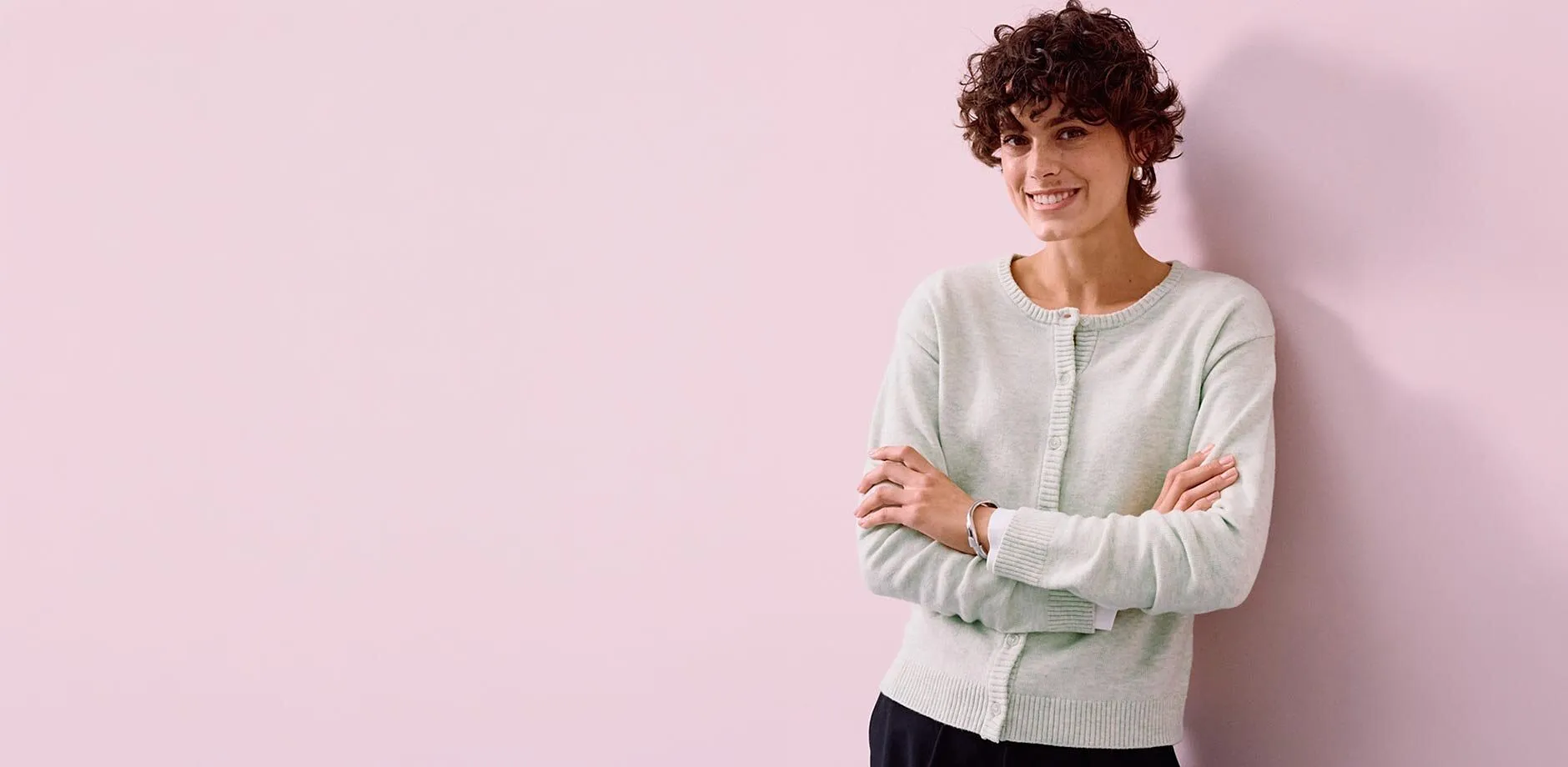 Sie tr&auml;gt eine hellgr&uuml;ne Strickjacke zur dunkle Hose.