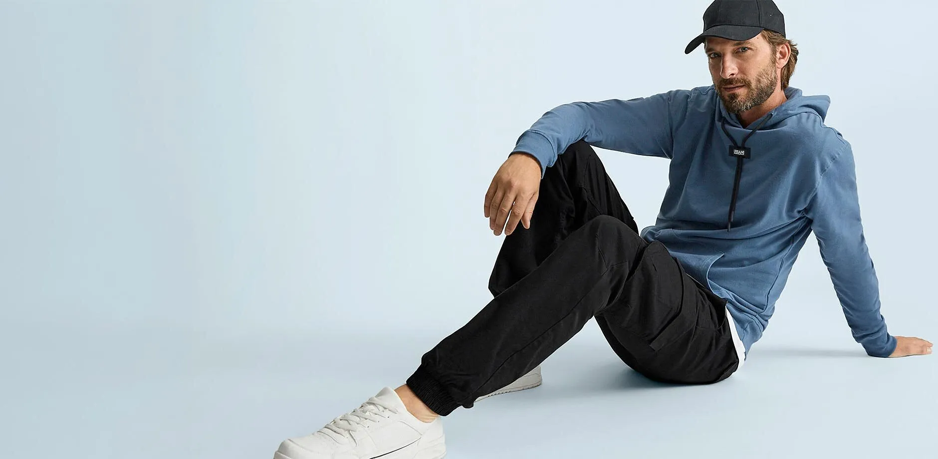Blaue Kapuzenjacke, schwarze Cargohose, wei&szlig;e Sneaker und schwarze Kappe f&uuml;r einen l&auml;ssigen Stil.